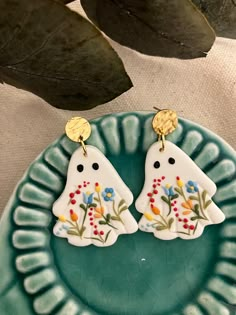 two white ceramic birds with flowers on them are sitting on a plate next to a plant