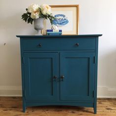 a blue cabinet with two doors and flowers on top in front of a white wall