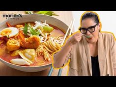 a woman holding chopsticks in front of a bowl of seafood and noodle soup