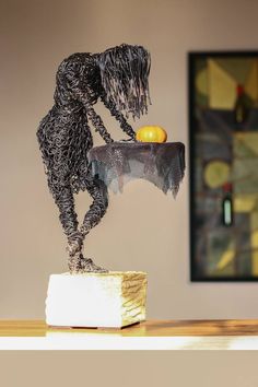 a sculpture of a person bending over to pick up an orange