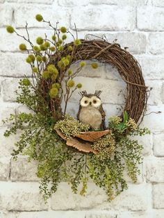 an owl is sitting in the middle of a wreath with greenery around it on a brick wall