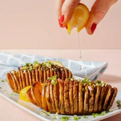 a person holding a lemon over some potato wedges on a white plate with green garnishes