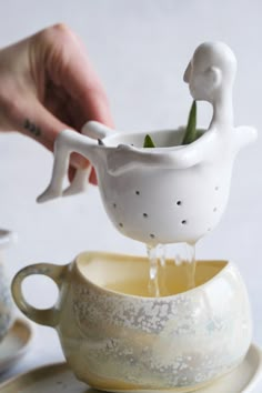 a person pouring water into a teacup with two swans on the cup and saucer