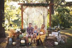 two children sitting on a bench in front of an outdoor backdrop with pumpkins and hay