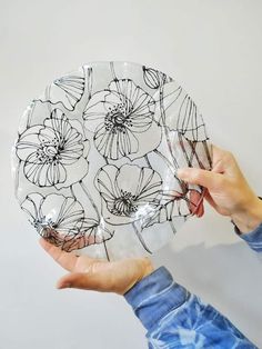 a person holding a glass plate with flowers drawn on it