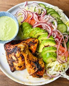 a white plate topped with chicken and veggies next to a bowl of dressing