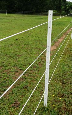 a white wire fence in the middle of a grassy field