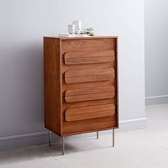 a tall wooden cabinet with five drawers on one side and two vases on the other