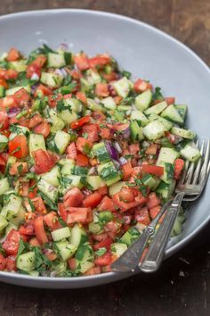 a bowl filled with cucumber and tomato salad on top of a wooden table