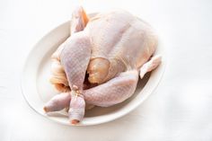 a whole chicken on a white plate sitting on a counter top with the skin still attached