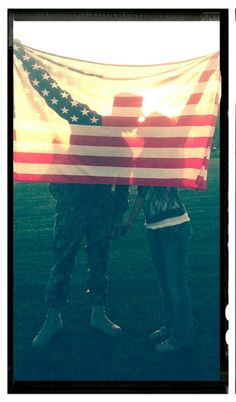 two people standing next to each other holding an american flag