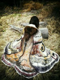 a woman sitting on top of a grass covered field next to a fallen tree trunk