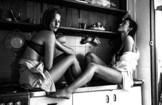 two women sitting on top of a stove in a kitchen next to each other,