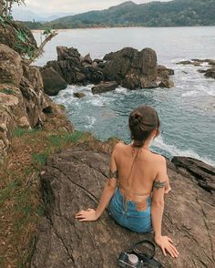 a woman sitting on top of a rock next to the ocean