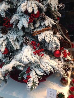 a white christmas tree with red berries and pine cones on display in a store window