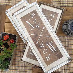 two framed clocks sitting on top of a wooden table next to flowers and a potted plant