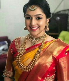 a woman in a red and yellow saree smiles at the camera with her hand on her hip