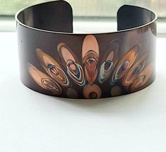 "This unique copper bracelet is made by painting patterns onto copper with a torch, and as the copper heats and cools it turns different colors naturally! Its quite an amazing process. the cuff is 1\" wide and is flexible enough so that you can make it fit your wrist. It is protected with a sealant to keep it from further oxidizing. These are custom made per order, so please keep in mind that with this process, nature is in charge of the colors, so see each one that I make is unique and cannot b Brown Copper Cuff Bracelet As Gift, Handmade Unique Copper Bangle, Unique Handmade Copper Bangle, Handmade Artistic Copper Bracelet, Handmade Artistic Copper Bracelets, Artistic Copper Cuff Bracelet, Artistic Copper Cuff Bracelet Bangle, Artistic Copper Cuff Bangle Bracelet, Copper Cuff Bracelet Wearable Art Gift