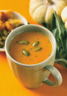 a cup of pumpkin soup on a yellow table next to some pumpkins and squash