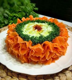 an orange and green cake on a white plate next to some greens in the background