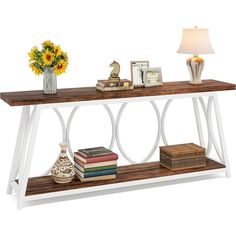 a white and wood console table with books, vases and flowers on it next to a lamp