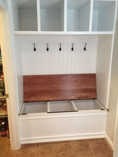 a white bench with wooden seat and hooks on it's back wall in a kitchen