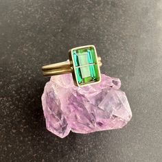 You won't be able to take your eyes off of this radiant cut green tourmaline ring. Aptly named, this stone radiates an array vibrant green hues. The double band compliments the crossbar and provides a luxurious contrast to the stone's geometric and longitudinal facets. A true one of a kind. 18k gold. 2.42 carat radiant cut green tourmaline. Size 7. Green Emerald Cut Multi-stone Jewelry, Emerald Cut Tourmaline Ring Fine Jewelry, Emerald Cut Tourmaline Ring In Fine Jewelry Style, Green Emerald Rectangular Stone Jewelry, Fine Jewelry Green Topaz Ring Emerald Cut, Emerald Cut Tourmaline Gemstone Rings, Green Topaz Emerald-cut Ring, Green Topaz Emerald Cut Ring, Emerald Cut Tourmaline Jewelry With Accent Stones