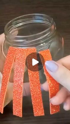 someone is holding an orange ribbon in front of a jar with some glitter on it