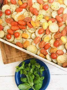 a pan filled with potatoes and tomatoes on top of a wooden cutting board next to a blue plate