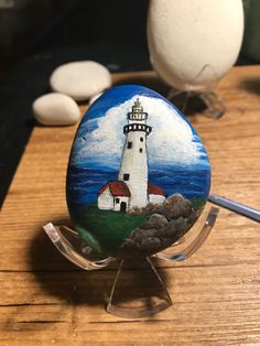 a painted rock with a lighthouse on it sitting on a wooden table next to eggs