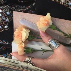 a woman's hand holding some flowers on top of a book