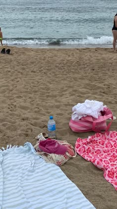 towels and blankets are laid out on the sand at the beach with people in the background