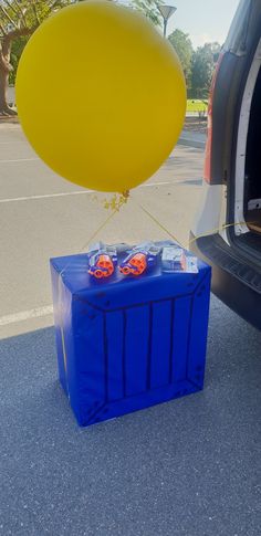 the trunk of a car with balloons attached to it is in front of a blue box