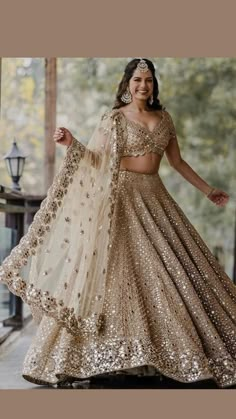 a woman in a gold and white lehenga is posing for the camera with her arms outstretched