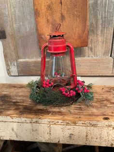 an old red lantern is sitting on top of a wooden table with berries and greenery