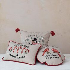 three decorative pillows on a white surface with red pom - poms around them