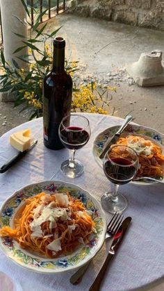 two plates of spaghetti and wine on a table outside