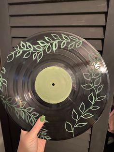 a hand holding a black and green record with leaves painted on it