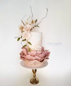 a white and pink wedding cake with flowers on the top is sitting on a gold pedestal