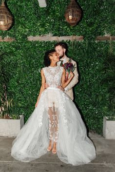 a bride and groom kissing in front of a wall covered with greenery at their wedding