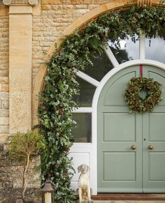 a dog sitting in front of a door with wreaths on it's side