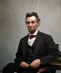 an old man in a suit and bow tie sitting on a chair with his hands crossed