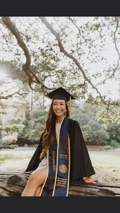 a woman sitting on top of a log wearing a graduation cap and gown