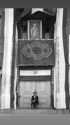 an old photo of a man sitting in front of a building with curtains on it