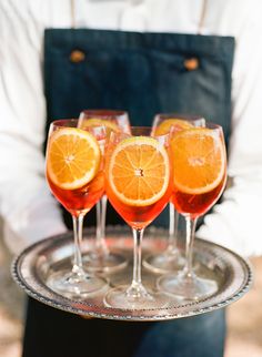 three glasses of wine with orange slices on a silver tray in front of a man