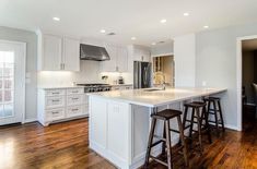 a large kitchen with white cabinets and wood flooring, along with two bar stools