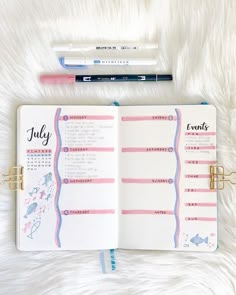 an open planner with pink and blue trims on it, next to a pen