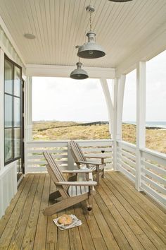 a porch with two chairs and a lamp on the ceiling above it, overlooking an ocean