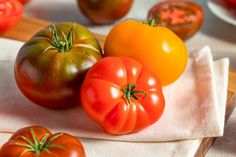 three tomatoes on a white cloth next to some other fruits and vegetables in the background