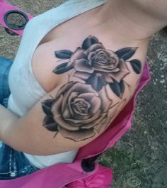 a woman with a rose tattoo on her shoulder and chest is sitting in the grass